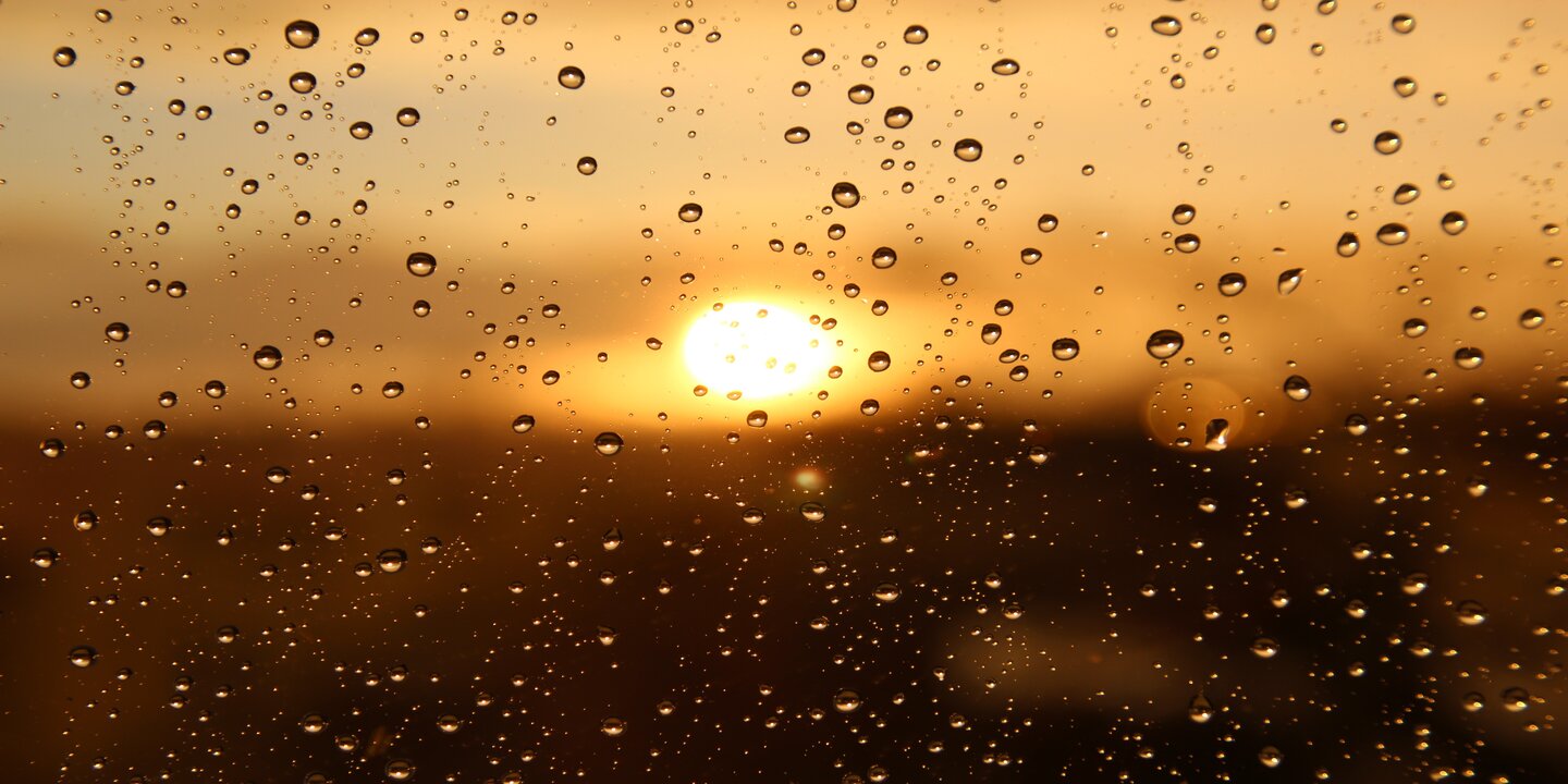 Regentropfen auf einem Fenster, durch das man die Sonne sehen kann