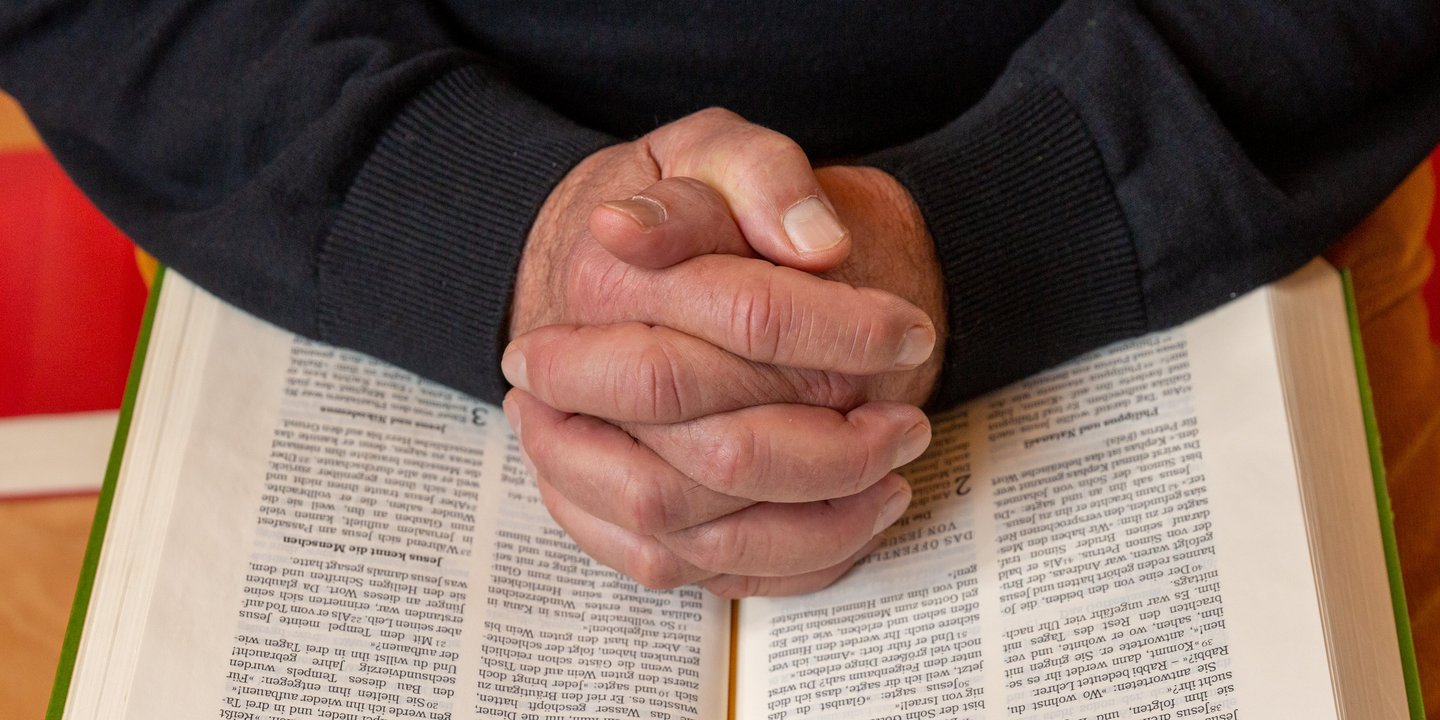 Zum Gebet gefaltete Hände liegen auf einer Bibel.