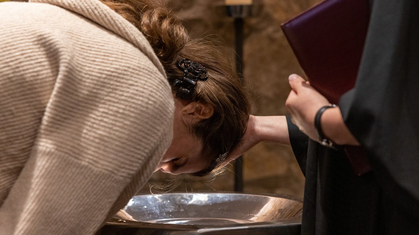 Eine Frau beugt sich für die Taufe über das Taufbecken.