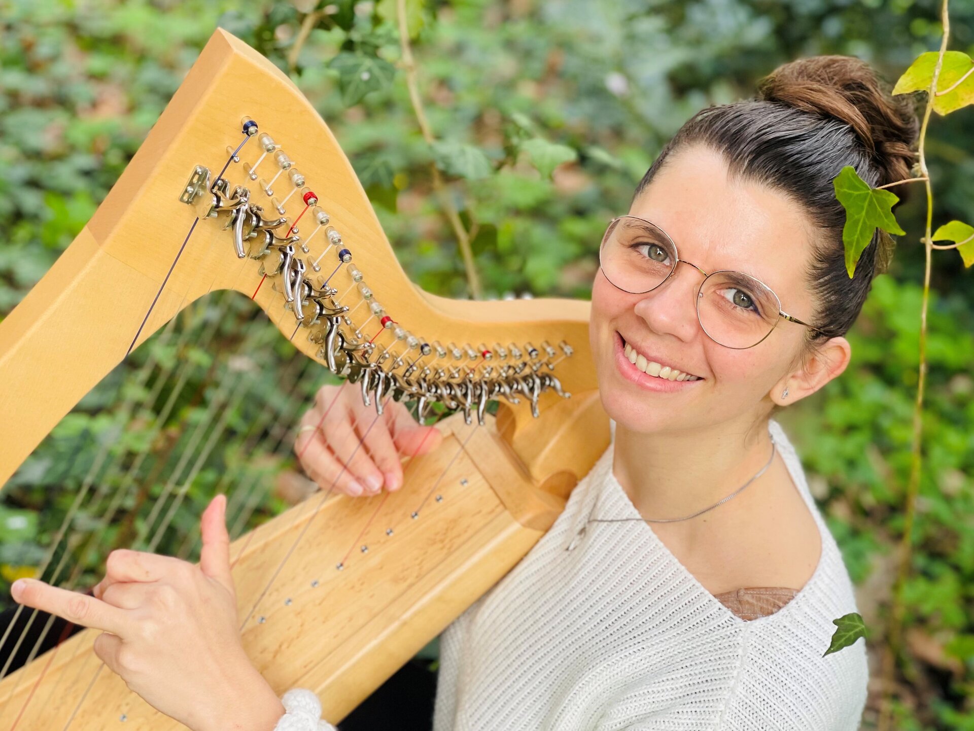 Eine Frau mit Brille spielt Harfe und lächelt in die Kamera