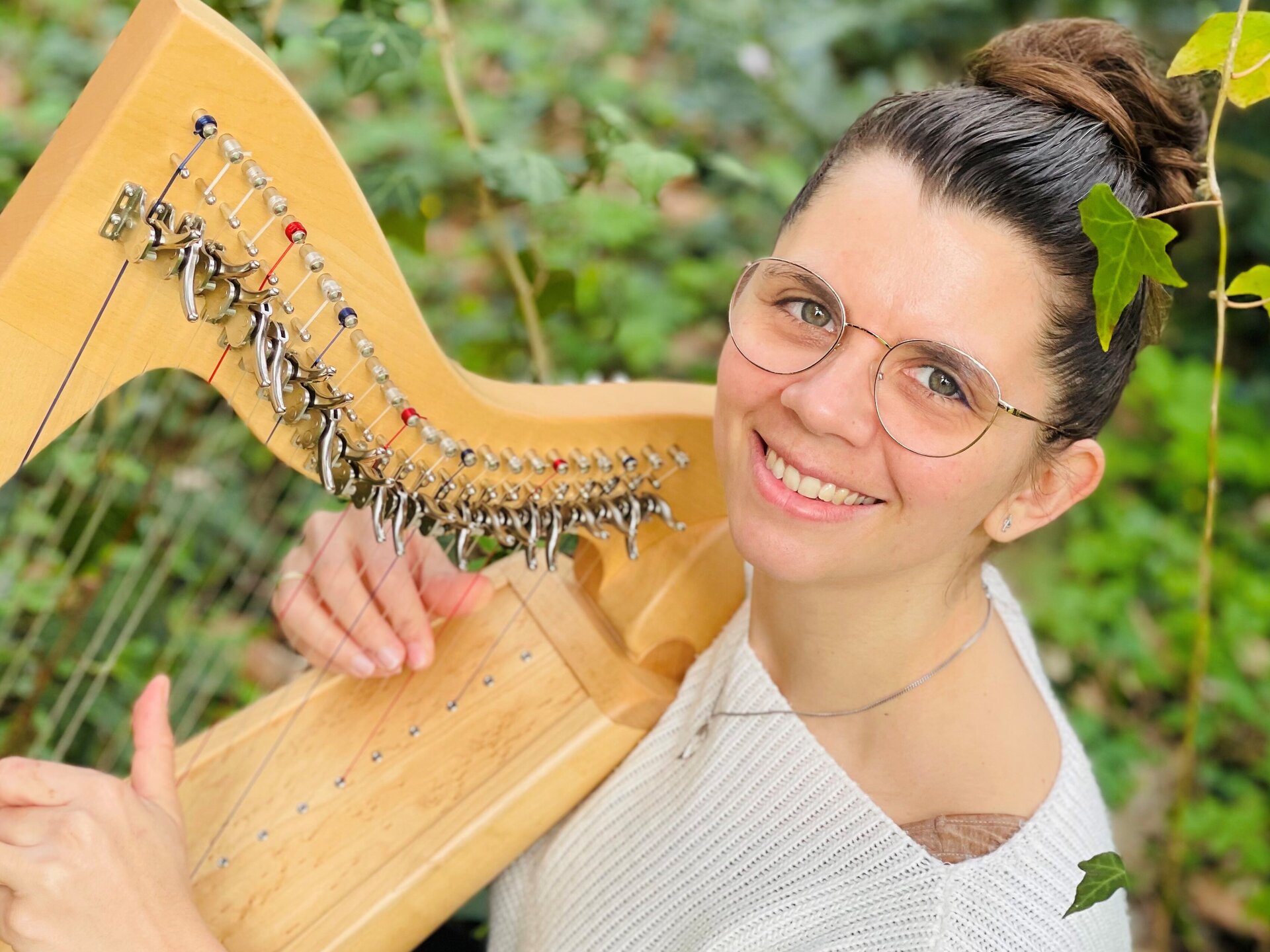 Eine Frau mit Brille spielt Harfe und lächelt in die Kamera