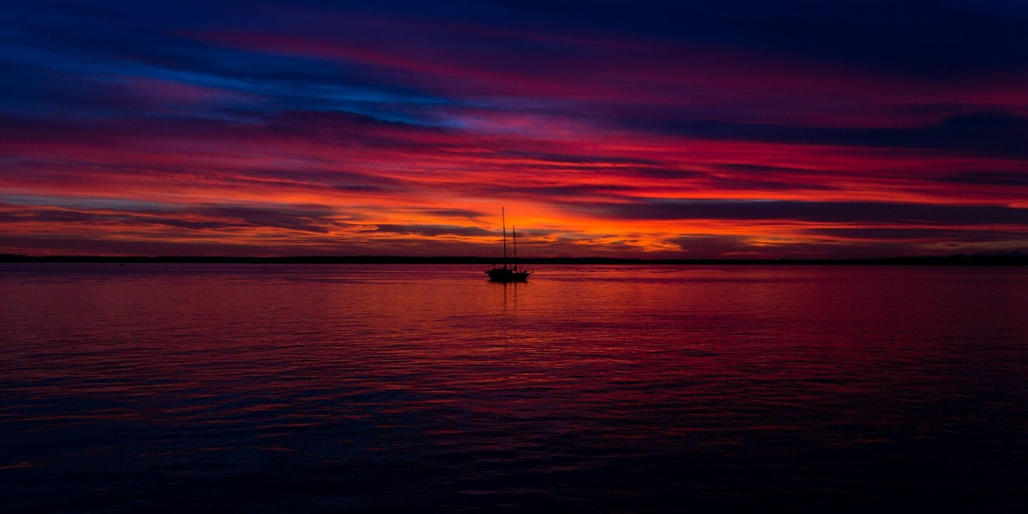 Sonnenuntergang Ein Segelboot vor dem rot-violetten Himmel des Sonnenuntergangs