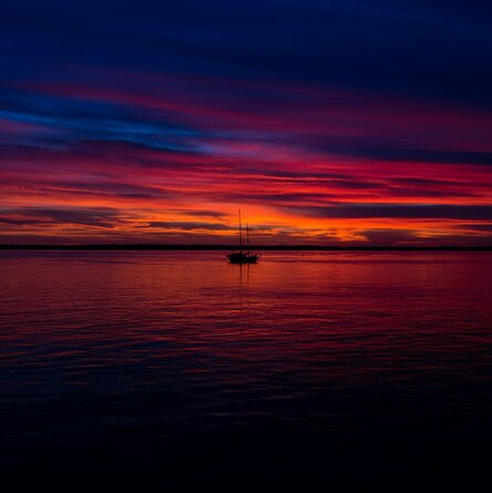 Ein Segelboot vor dem rot-violetten Himmel des Sonnenuntergangs