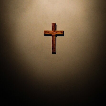 Ein kleines Kreuz in einem Lichtkegel an einer dunklen Wand.