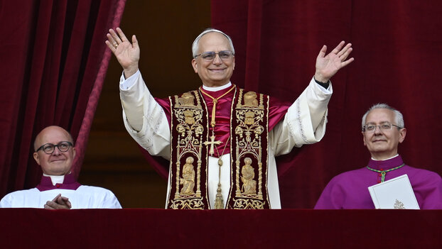 Ein grauhaariger Mann im weißen Papstgewand mit rot-goldener Stola winkt