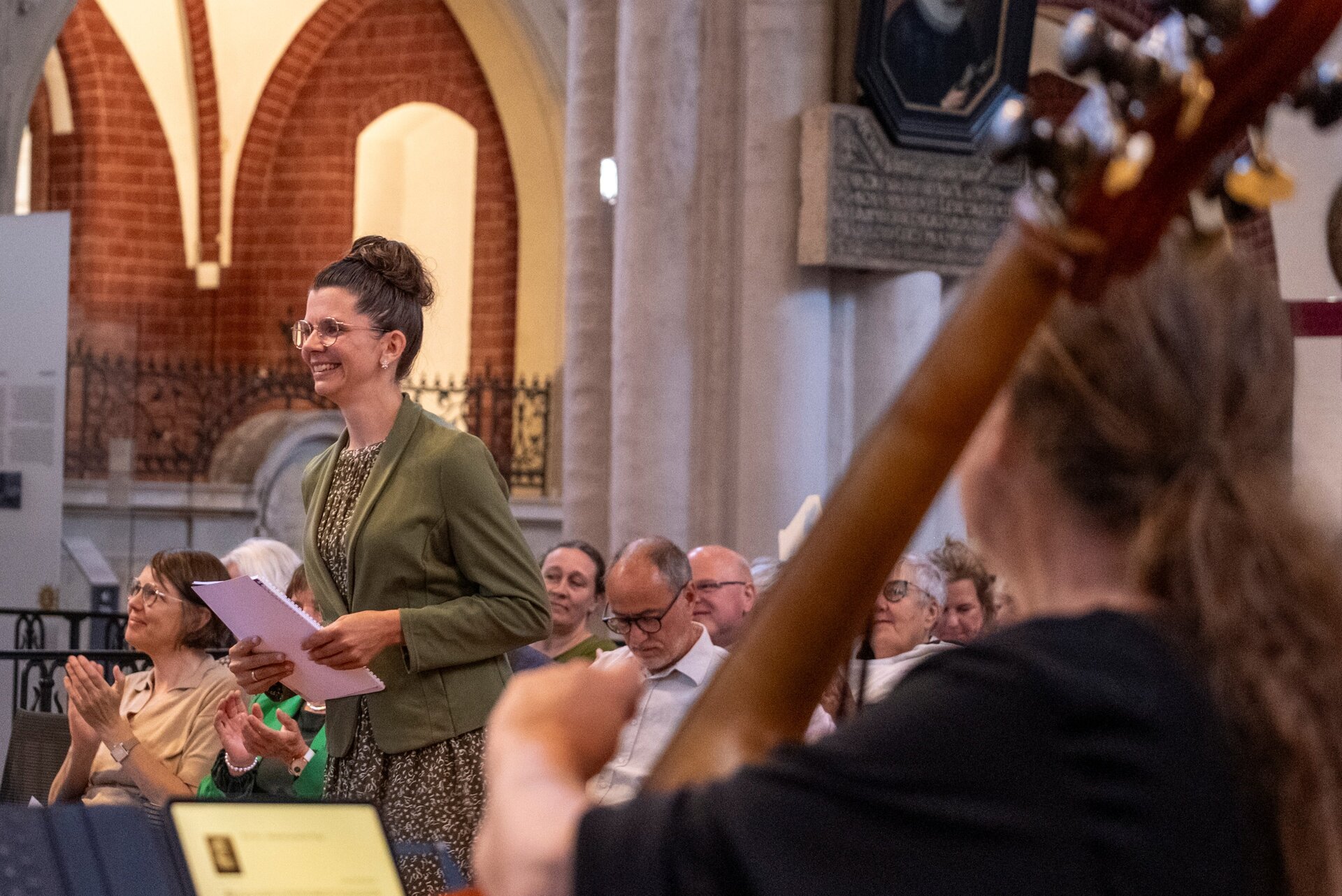 Eine Frau mit grünem Blazer steht lächelnd in einer Kirche.