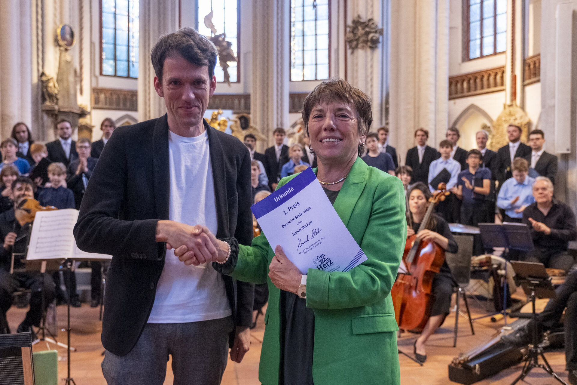 Ein Mann in schwarzem Sakko reicht einer Frau in grünem Blazer die Hand.