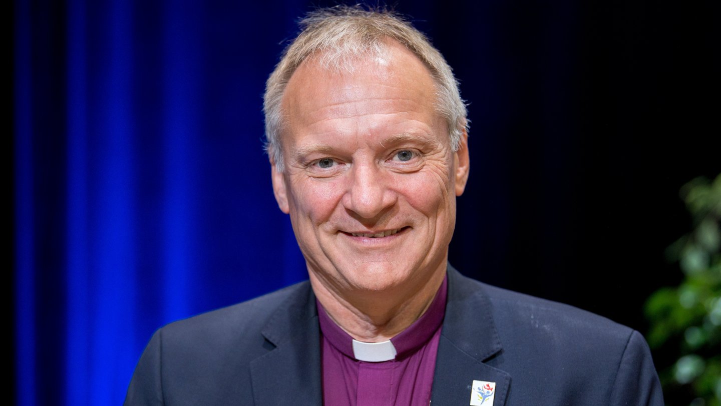 Ein freundlich blickender Mann im violetten Collar-Hemd und schwarzem Sakko. Das Bild zeigt den dänischen Bischof Henrik Stubkjær.