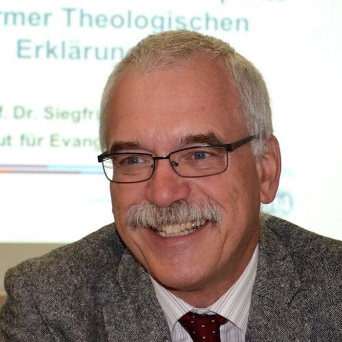 Ein Mann mit grauen Haaren, Brille und grauem Schnauzbart