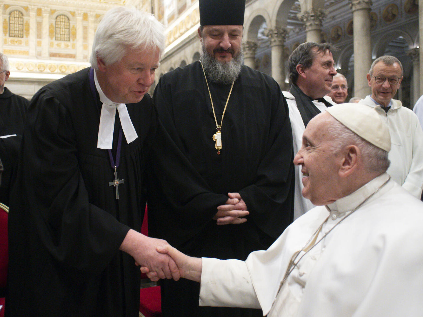 Ein evangelischer Pfarrer im schwarzen Talar reicht dem Papst in weißer Kleidung die Hand
