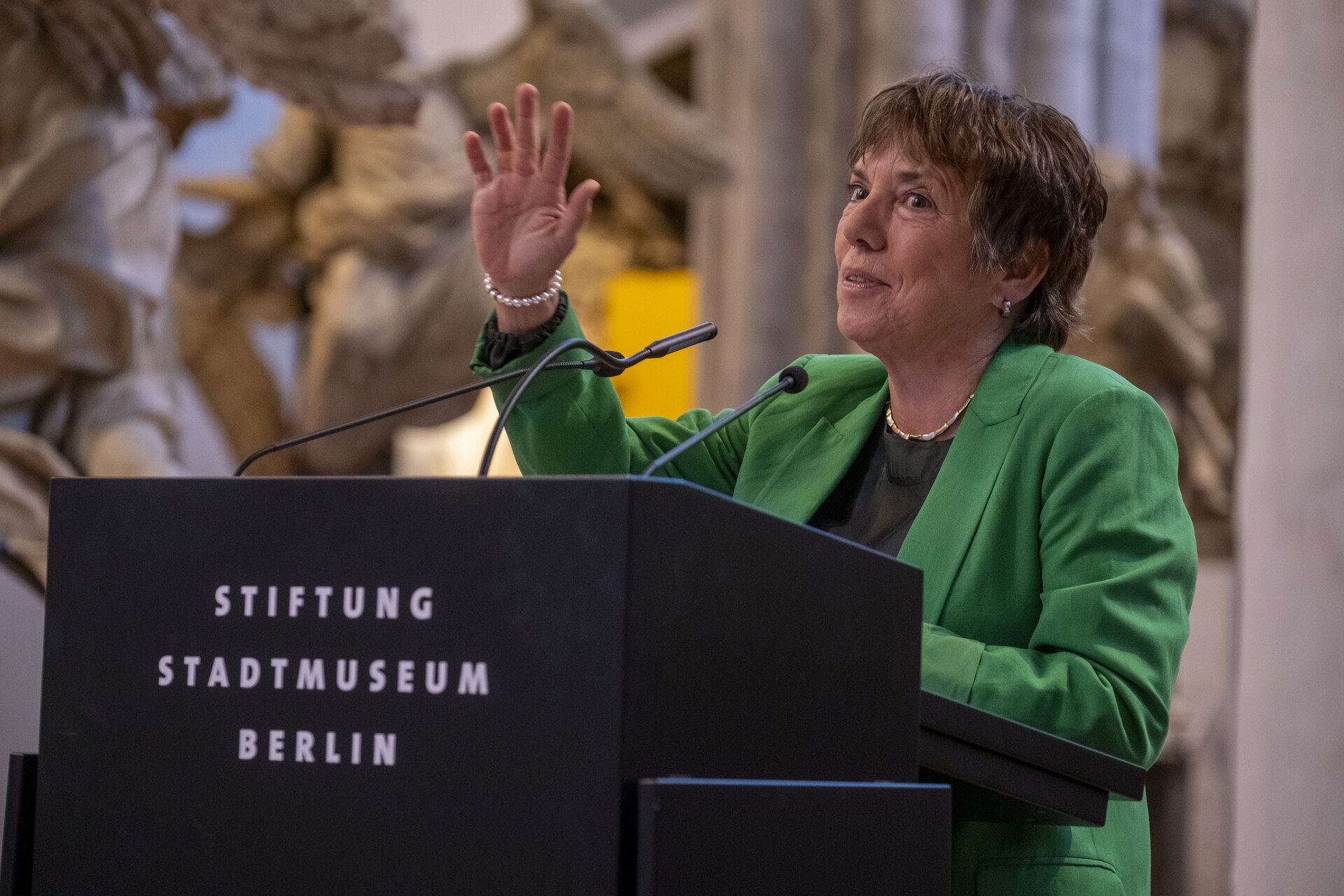 Eine Frau in grünem Blazer an einem Sprechpult.
