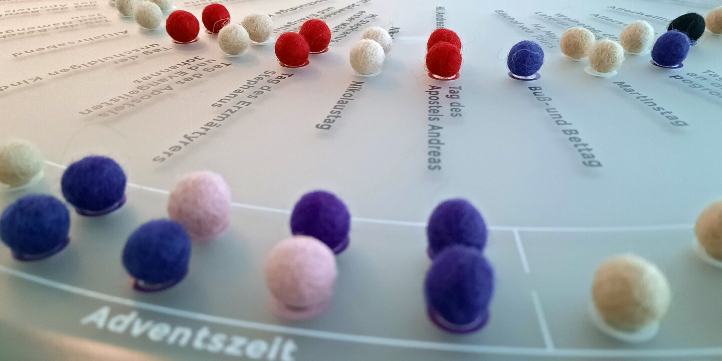 Bunte Filzkügelchen sind in mehreren Kreisen auf einer hellgrauen Fläche angeordnet.