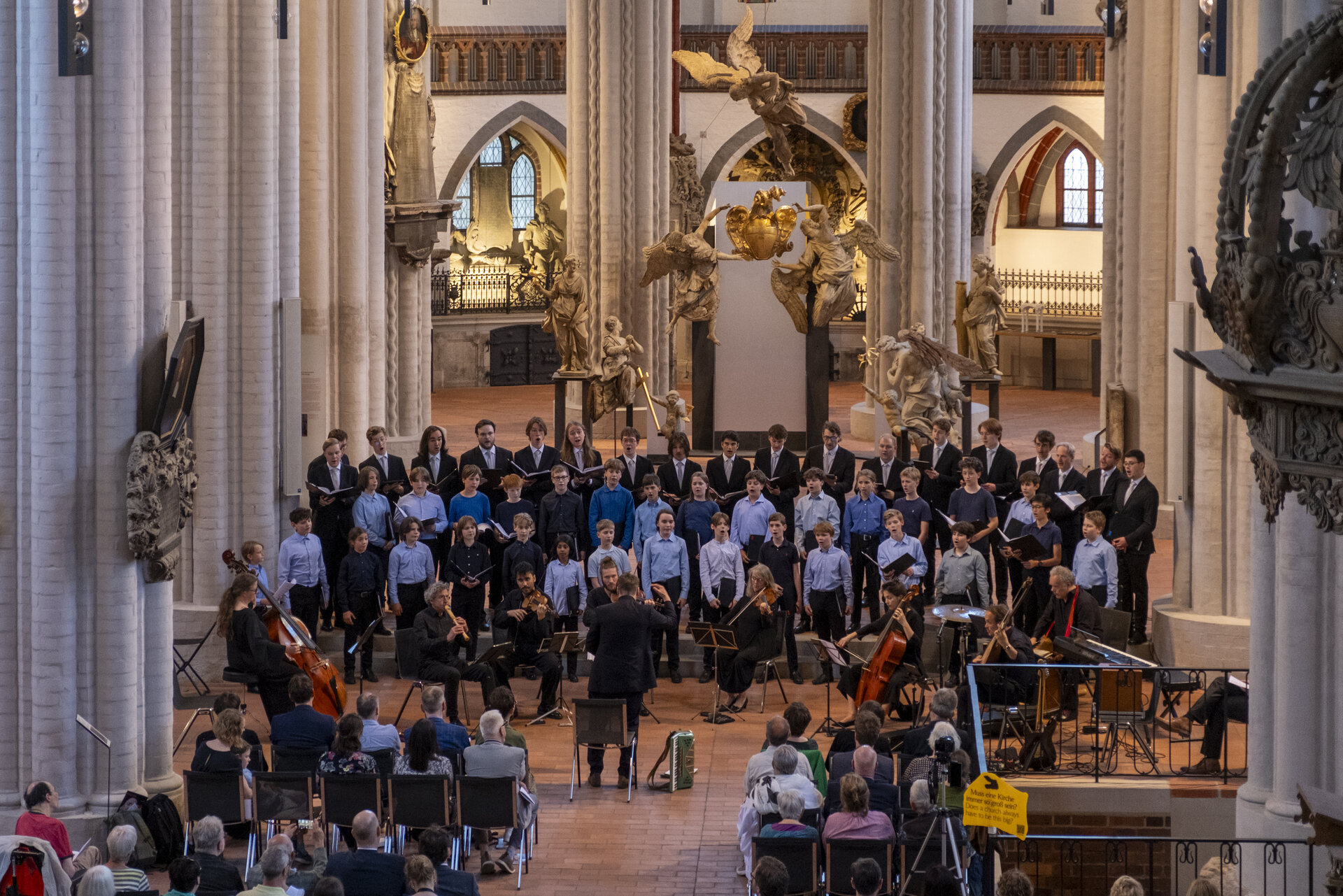 Blick in ein Kirchenschiff. Vorne steht ein großer Chor, davor sitzt ein kleines Orchester.