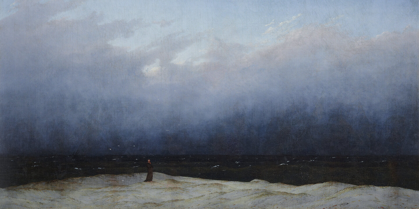 Gemälde in dominierenden Blau-Tönen. Die oberen 2/3 stellen einen teil-bewölkten Himmel dar, der am Horizont in ein fast schwarzes Meer übergeht. Am unteren Bildrand steht auf einem felsigen Ufer ein Mönch in schwarzer Kutte und blickt Richtung Meer.