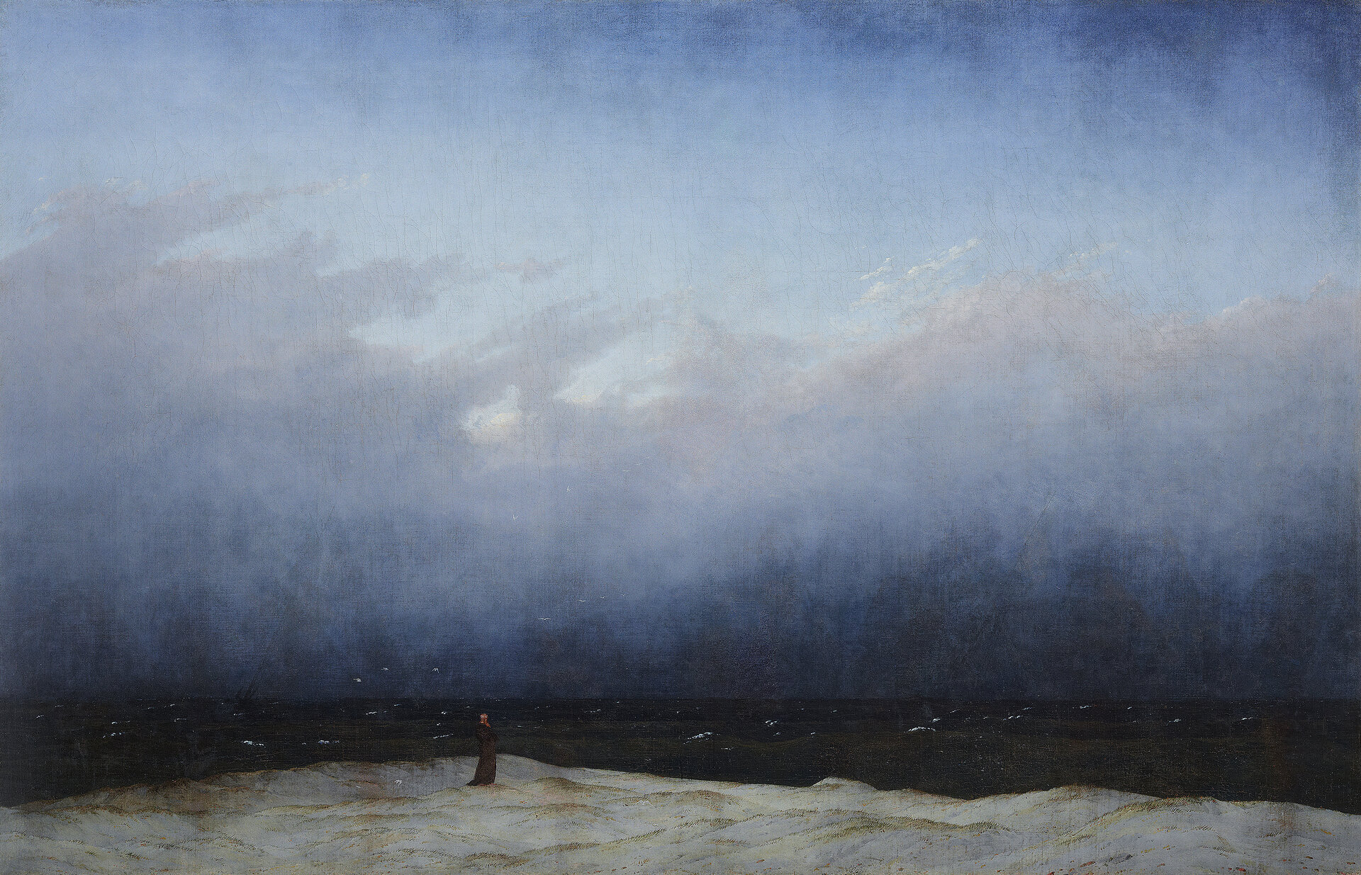 Gemälde in dominierenden Blau-Tönen. Die oberen 2/3 stellen einen teil-bewölkten Himmel dar, der am Horizont in ein fast schwarzes Meer übergeht. Am unteren Bildrand steht auf einem felsigen Ufer ein Mönch in schwarzer Kutte und blickt Richtung Meer.