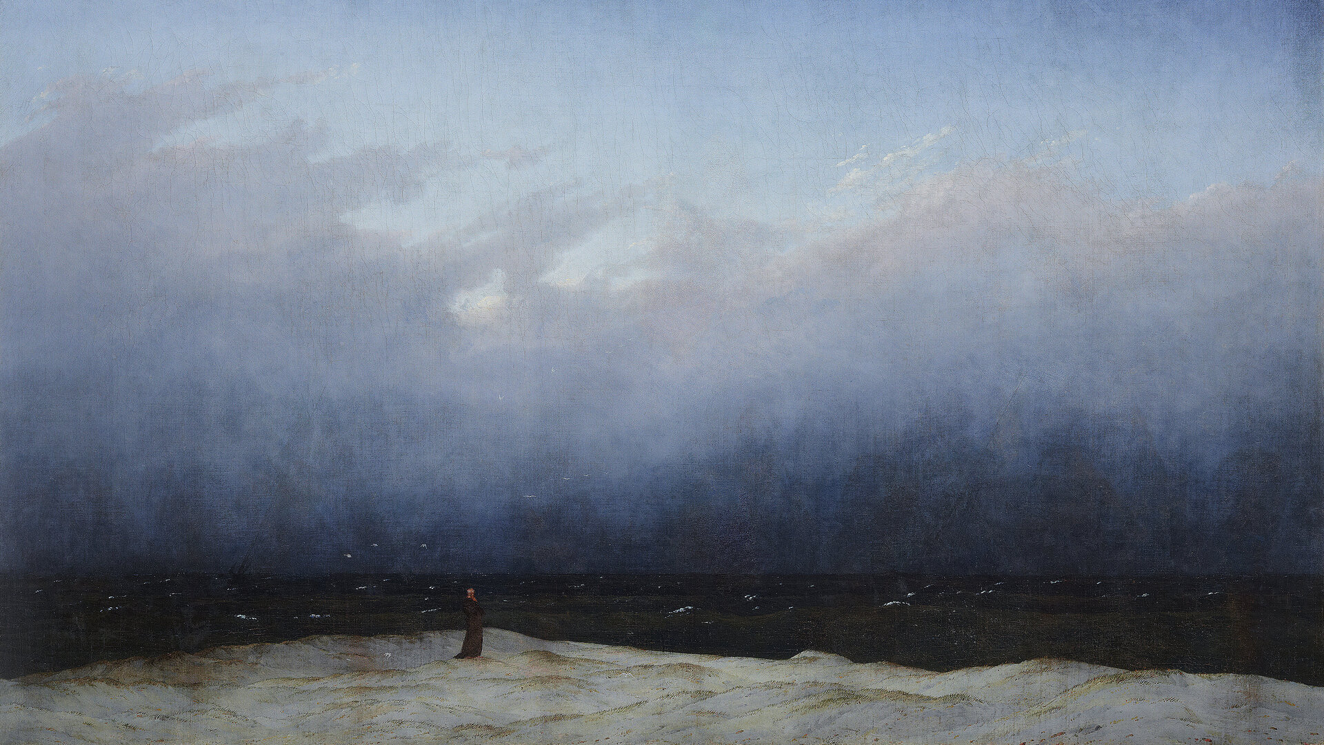 Gemälde in dominierenden Blau-Tönen. Die oberen 2/3 stellen einen teil-bewölkten Himmel dar, der am Horizont in ein fast schwarzes Meer übergeht. Am unteren Bildrand steht auf einem felsigen Ufer ein Mönch in schwarzer Kutte und blickt Richtung Meer.