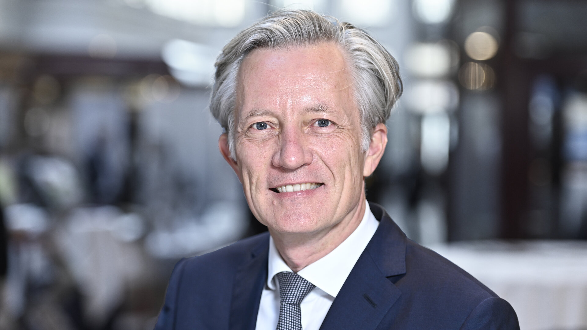 Ein Mann mit grauen Haaren und blauem Anzug lächelt in die Kamera